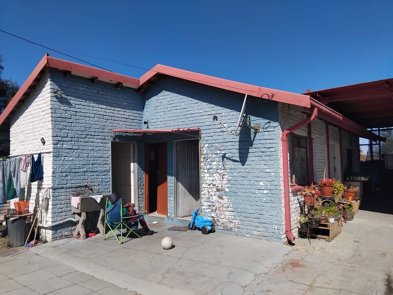 Rear view of a single-story brick house featuring a concrete patio area, metal roofing, and external wash basin.