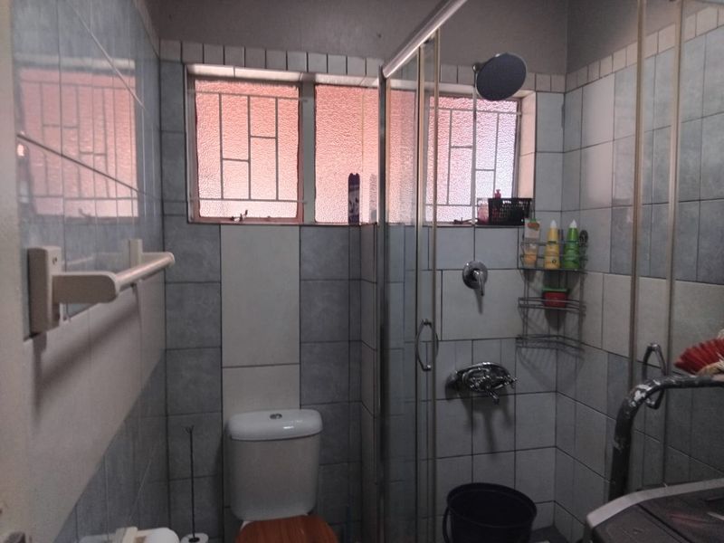 A functional bathroom featuring a shower enclosure, toilet, and tiled walls with security bars on the window.