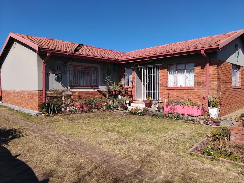 Front elevation of a single-story house featuring a tiled roof, brick and plaster facade, and a paved entrance walkway with a small front garden.