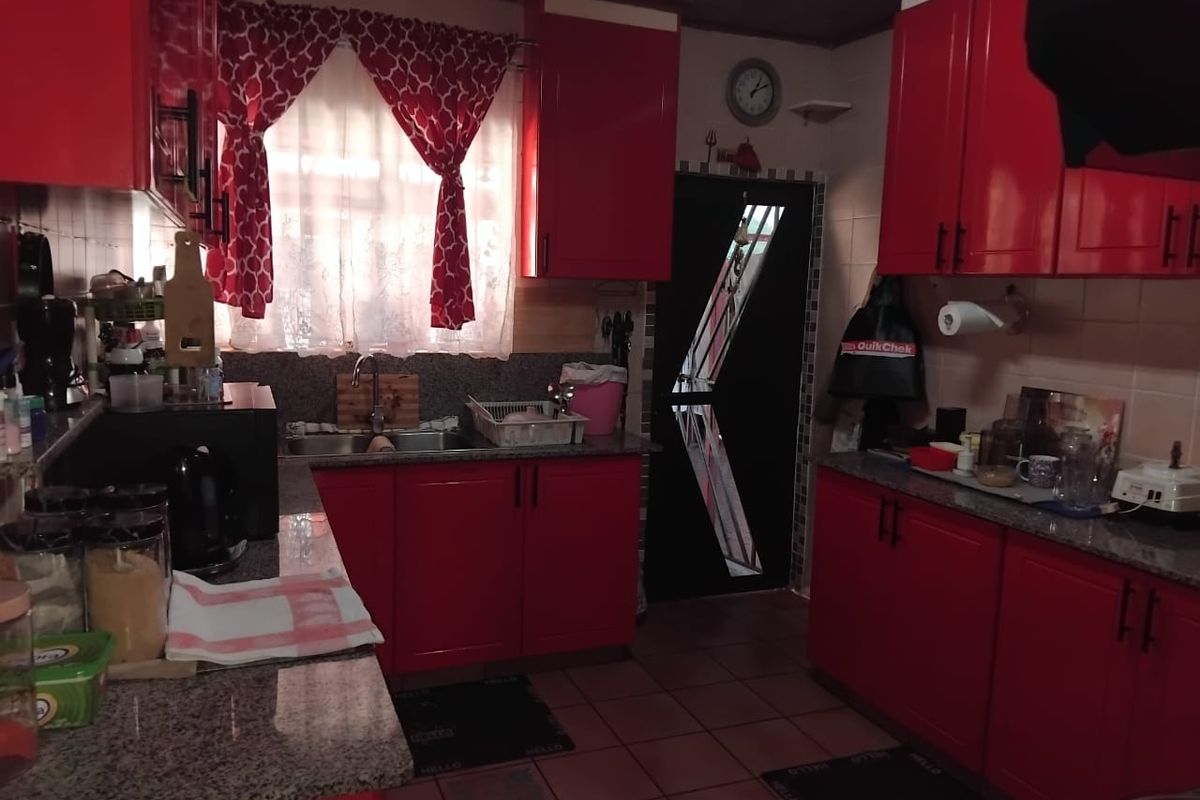 A functional kitchen featuring vibrant red cabinetry, granite countertops, a double basin sink, and tiled flooring with a practical layout.