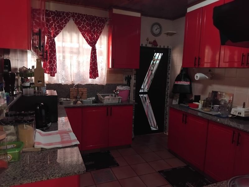 A functional kitchen featuring vibrant red cabinetry, granite countertops, a double basin sink, and tiled flooring with a practical layout.