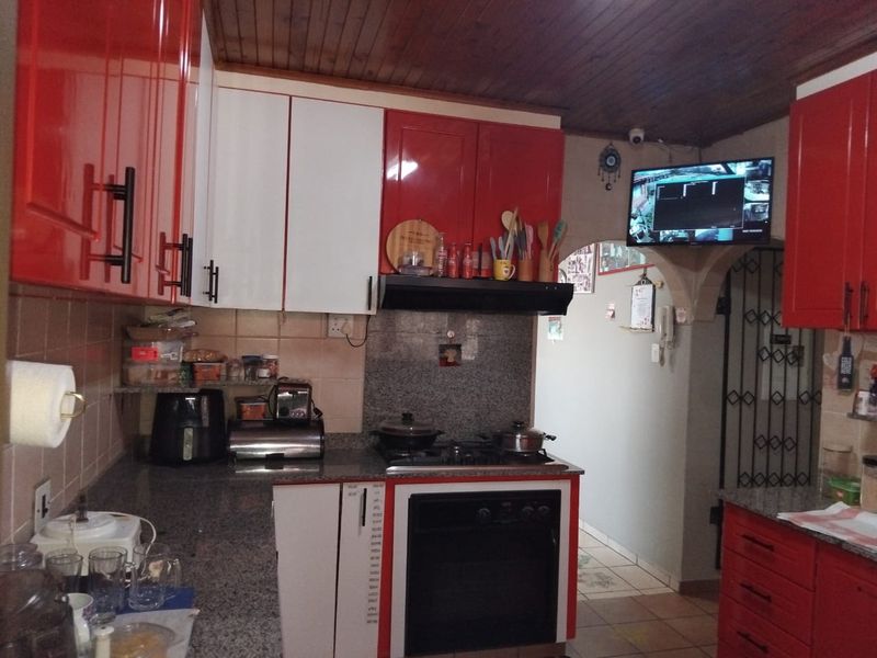 A functional kitchen featuring red and white cabinetry, granite countertops, a built-in oven with gas hob, and a distinctive timber-paneled ceiling.