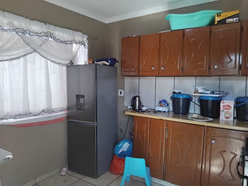 A functional kitchen featuring dated brown cabinetry, tiled backsplash, and laminate countertops, offering potential for modernization and aesthetic improvement.