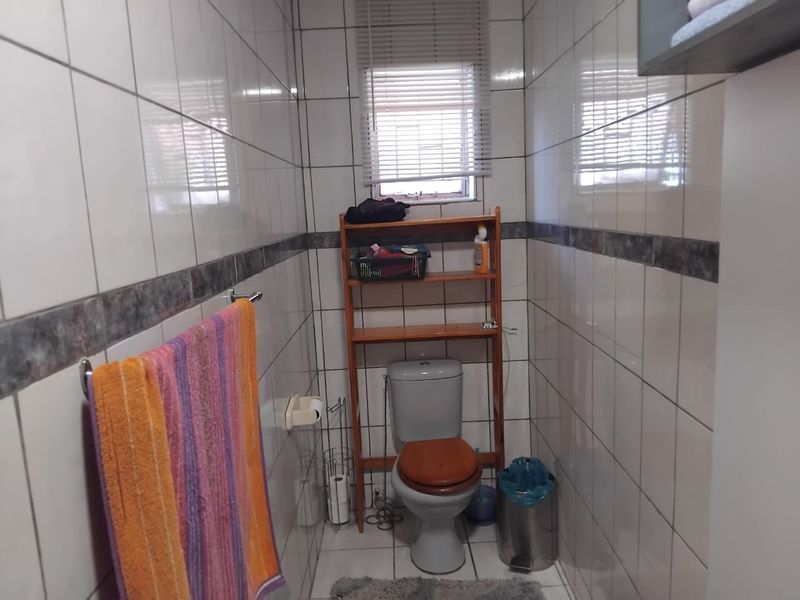 A compact bathroom featuring full-height wall tiling, a standard toilet, and a window with fitted blinds.