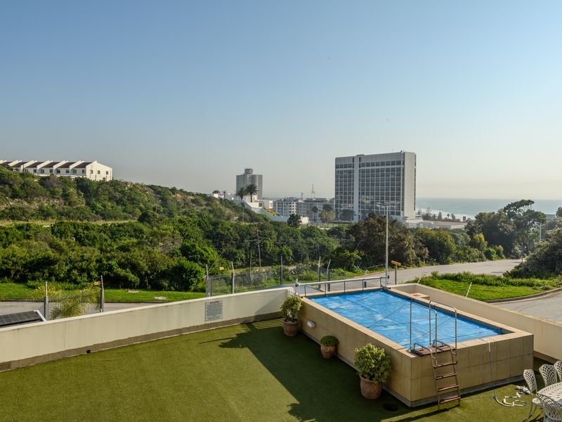 Elevated outdoor terrace featuring a raised swimming pool with cover, artificial turf surfacing, and expansive coastal and urban views.