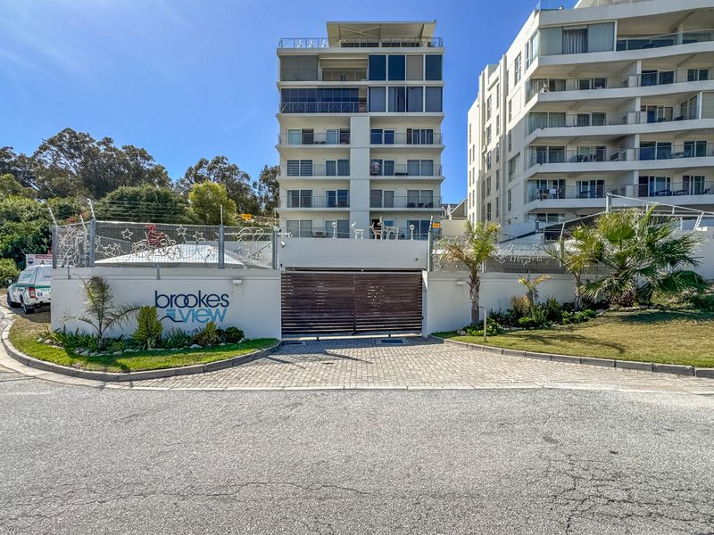Front exterior view of the Brookes View apartment complex, featuring a secure gated entrance, paved driveway, and well-maintained perimeter fencing.