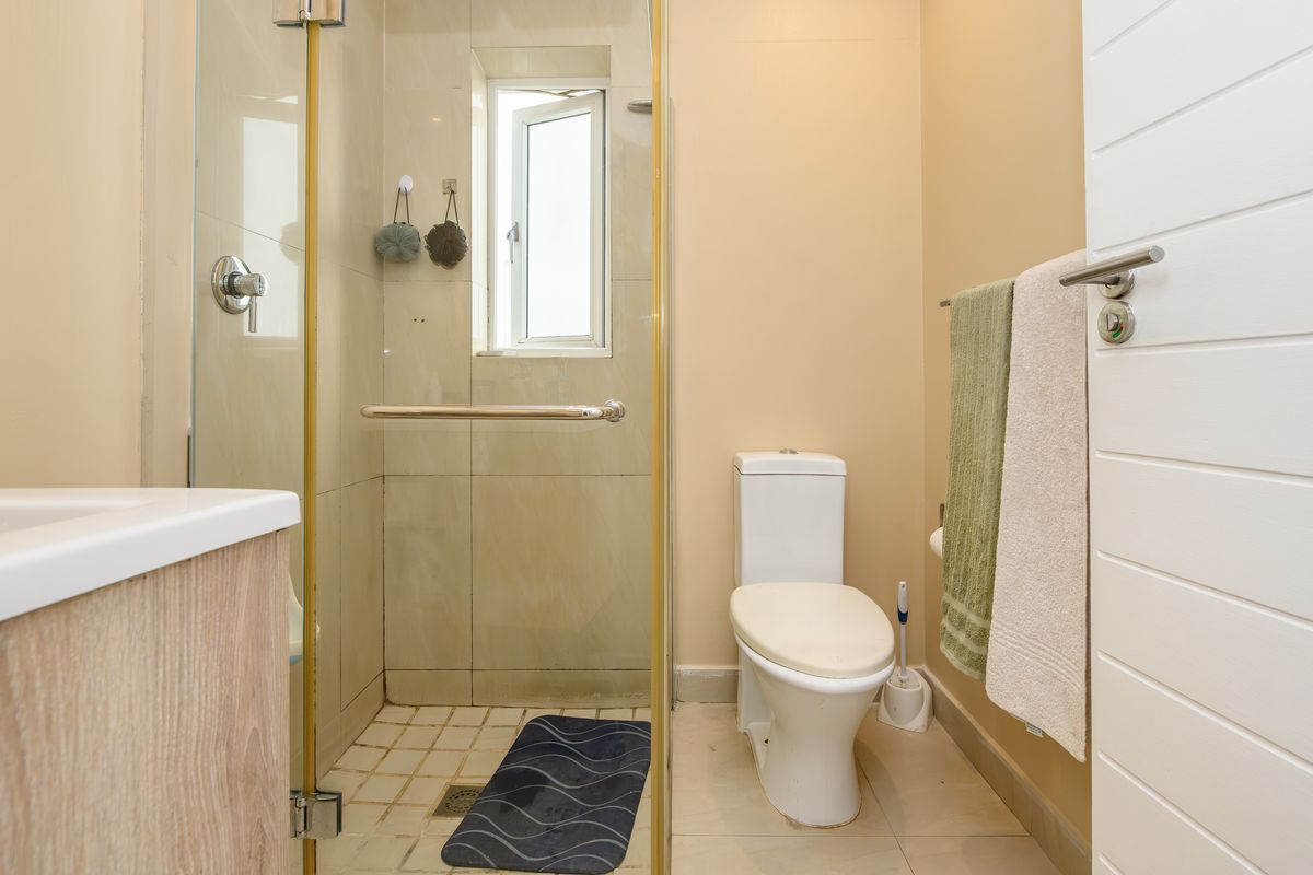 A functional bathroom featuring a glass-enclosed shower, tiled walls and flooring, and a standard toilet suite.