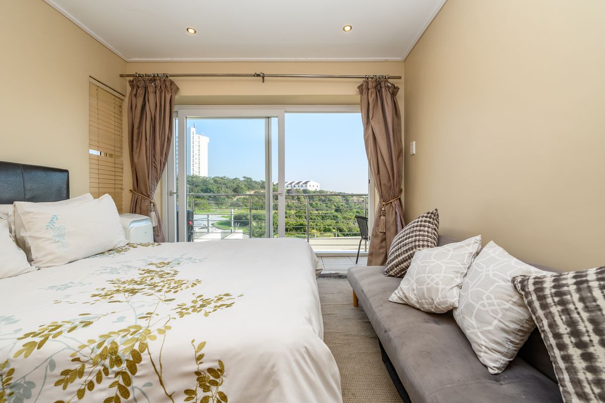 A well-lit bedroom featuring a sliding glass door that opens onto a balcony with scenic outdoor views.