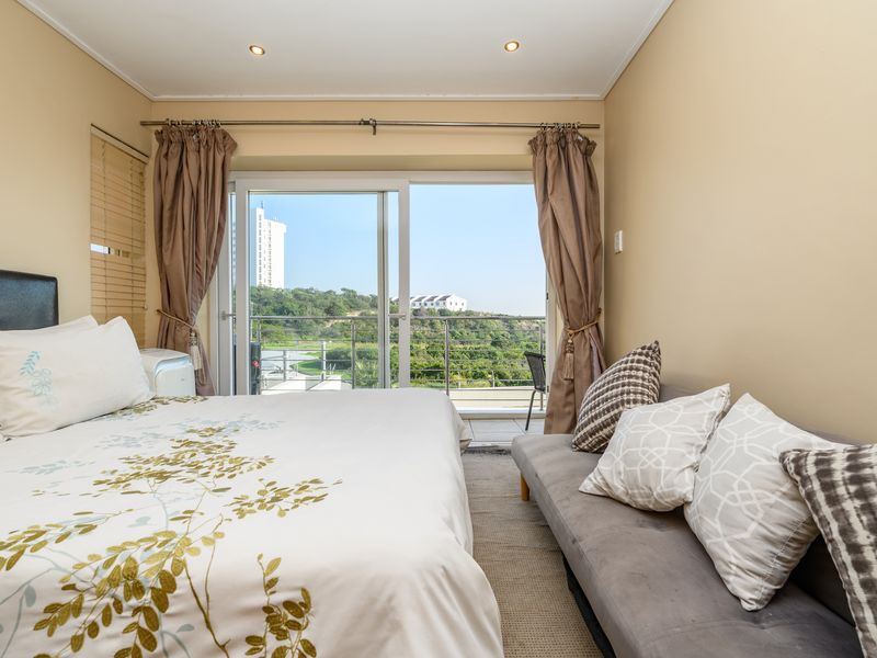 A well-lit bedroom featuring a sliding glass door that opens onto a balcony with scenic outdoor views.