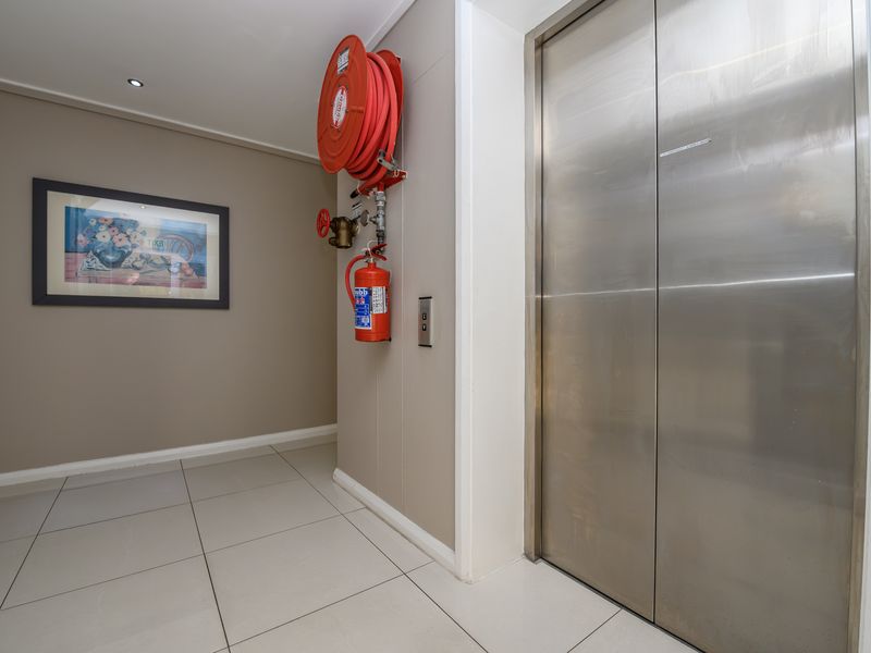 A clean and well-maintained apartment building hallway featuring stainless steel elevator doors and essential fire safety equipment.