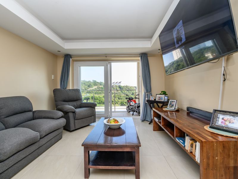 A comfortable living room featuring tiled flooring, a recessed ceiling, and a sliding glass door that provides direct access to the balcony.
