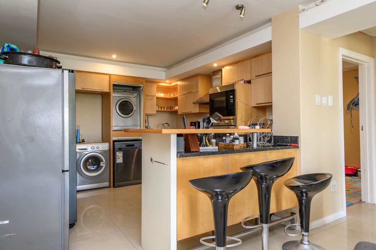 A functional kitchen featuring light wood cabinetry, granite countertops, a breakfast bar, and integrated appliances including an oven and extractor fan.