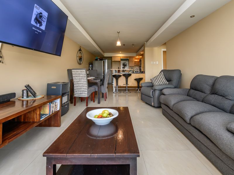 An open-plan living and kitchen area featuring tiled flooring, recessed lighting, and a functional kitchen layout with a breakfast bar.