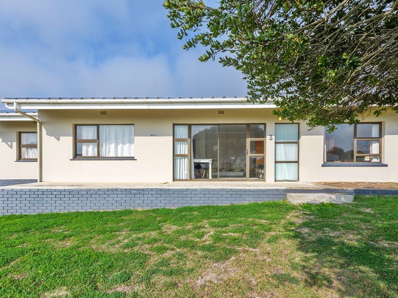 Rear elevation of the house featuring a paved patio area, sliding glass doors, and aluminium window frames set against a lawned garden.