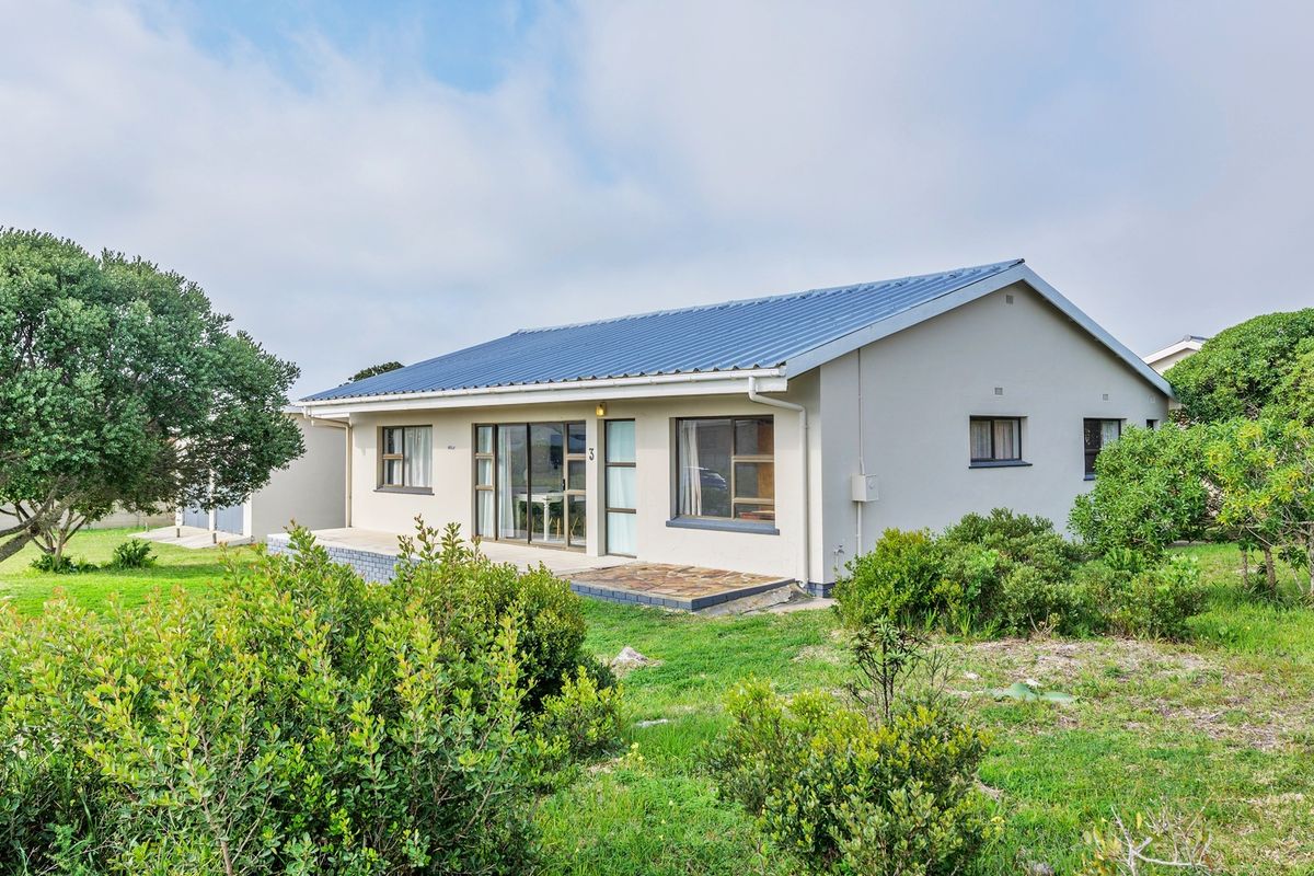 Rear view of a single-story house featuring a metal roof, sliding glass doors, and a small stone patio set within a garden.