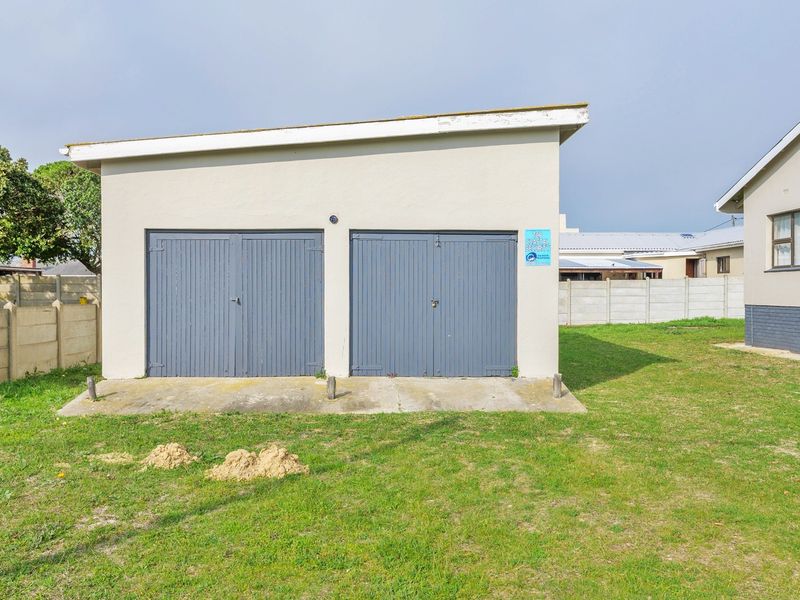 A detached double garage featuring grey timber-style doors, set within a spacious garden area with a precast concrete boundary wall.