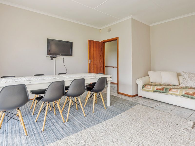 A functional living and dining area featuring tiled flooring, neutral walls, and a timber door leading to an adjacent space.