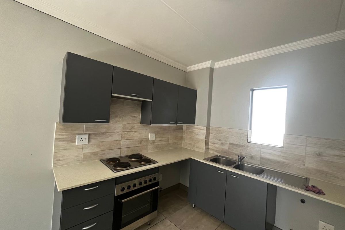 Modern kitchen featuring dark grey cabinetry, light stone-look countertops, tiled backsplash, built-in oven and hob, and a double sink with drainer.