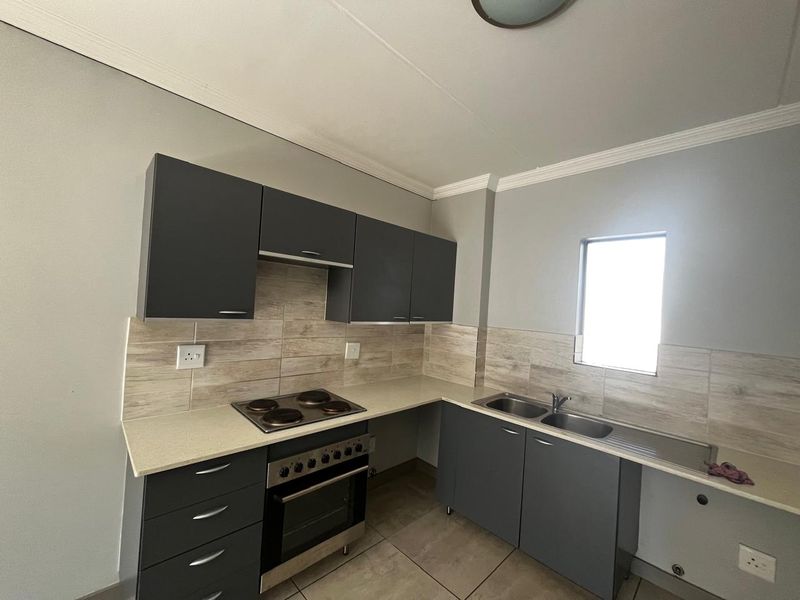 Modern kitchen featuring dark grey cabinetry, light stone-look countertops, tiled backsplash, built-in oven and hob, and a double sink with drainer.
