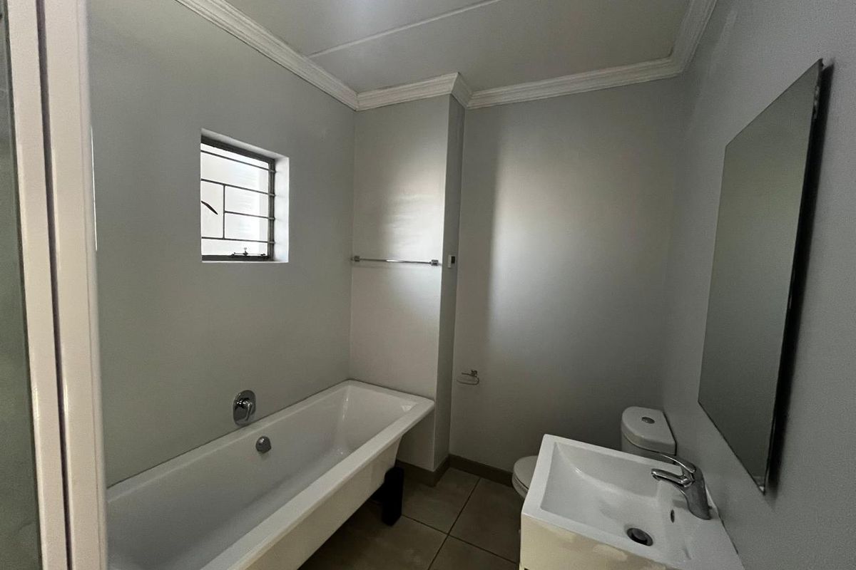 A clean, functional bathroom featuring a bathtub, vanity basin, and toilet, finished with neutral wall paint and tiled flooring.