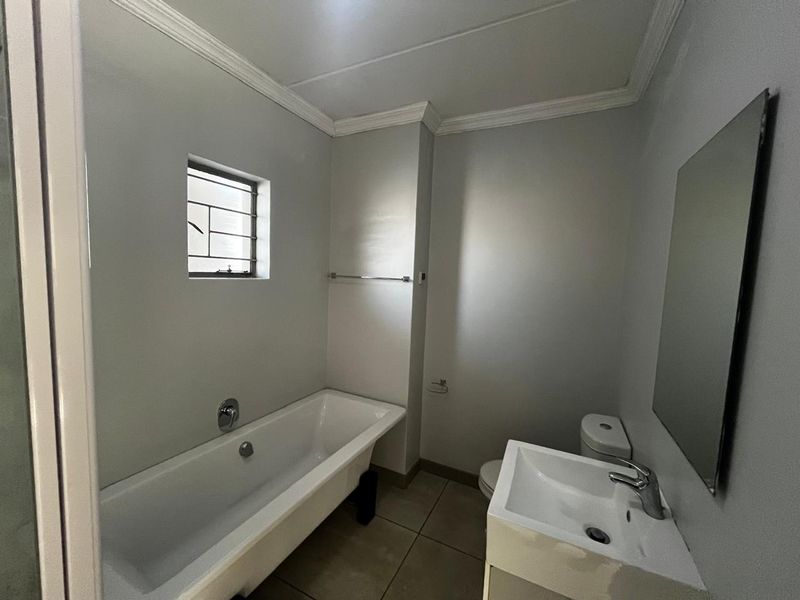 A clean, functional bathroom featuring a bathtub, vanity basin, and toilet, finished with neutral wall paint and tiled flooring.