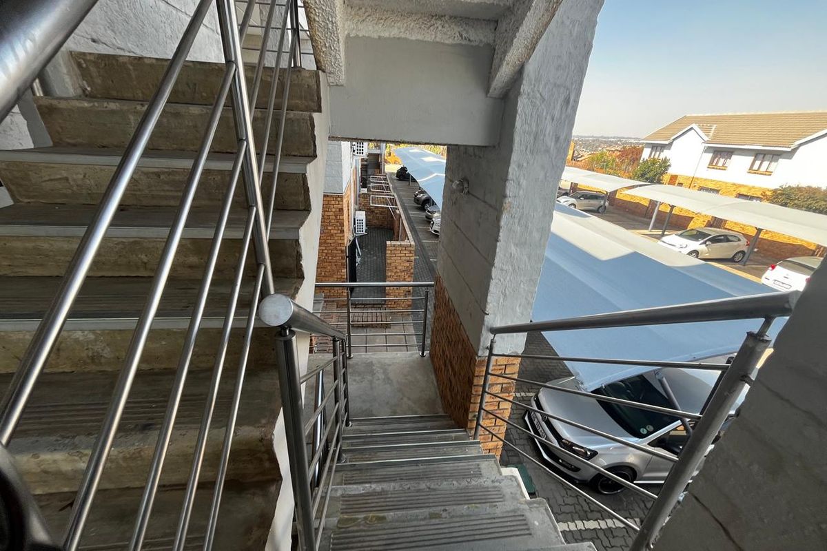 Exterior view of a concrete staircase with stainless steel railings, overlooking the apartment complex parking area and carports.