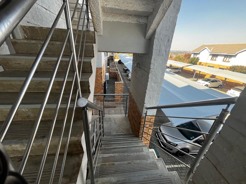 Exterior view of a concrete staircase with stainless steel railings, overlooking the apartment complex parking area and carports.