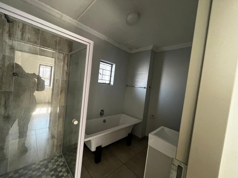 A functional bathroom featuring a separate shower enclosure, a classic freestanding bathtub, and a vanity basin with neutral floor tiling.