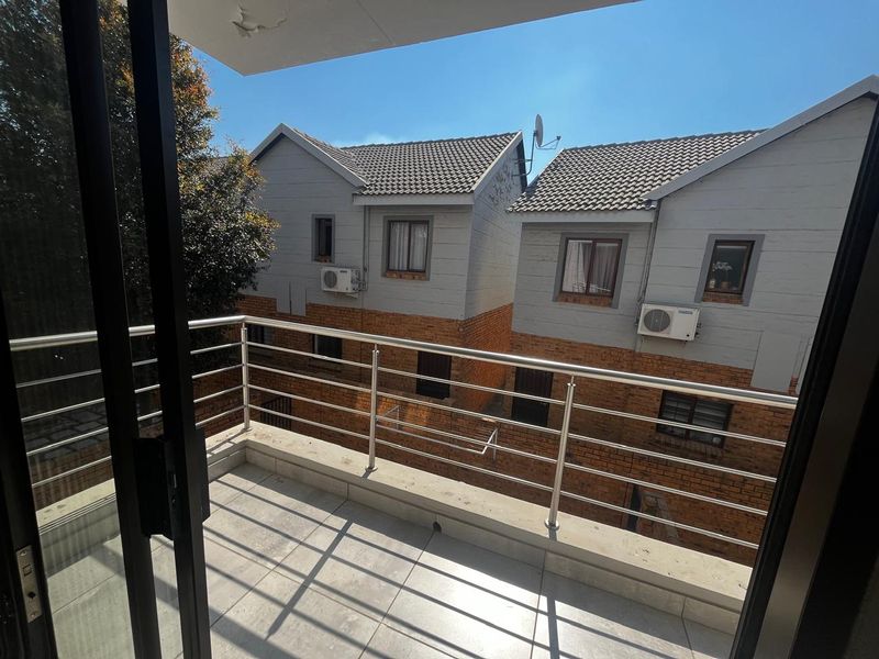 A private balcony featuring tiled flooring and a stainless steel balustrade, offering an elevated view of the surrounding apartment complex.