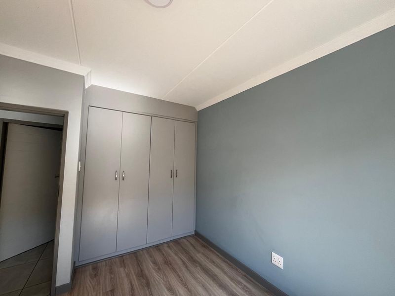 A clean, empty bedroom featuring modern laminate flooring, built-in cupboards, and a neutral grey accent wall.