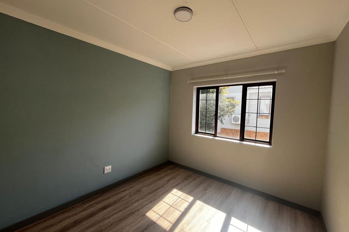 A bright, empty bedroom featuring modern laminate flooring, a dual-tone painted wall, and a window fitted with security bars.