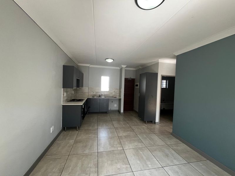 An open-plan kitchen area featuring modern grey cabinetry, tiled flooring, and neutral wall finishes, providing a clean and functional space.