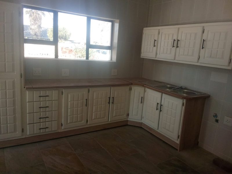 A functional kitchen featuring white cabinetry, tiled splashbacks, and a double sink, offering a clean and neutral space ready for personalization.