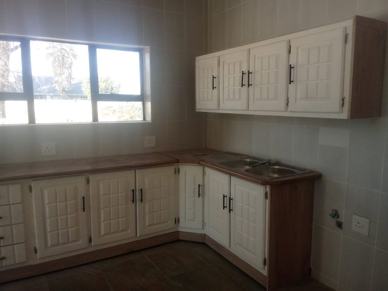 A functional kitchen space featuring white built-in cabinetry, a double bowl sink, tiled splashbacks, and ample countertop workspace with natural light.