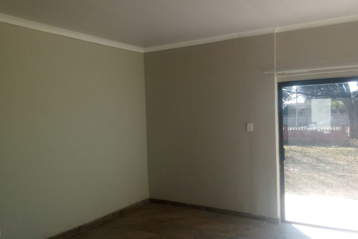 An empty living room featuring neutral painted walls, tiled flooring, and a sliding glass door providing access to the exterior.