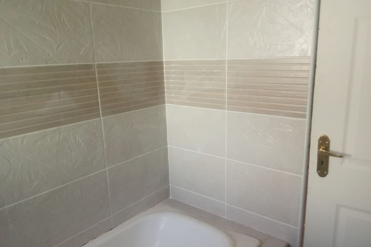A bathroom corner featuring a built-in bathtub with decorative ceramic wall tiling and a standard interior door.