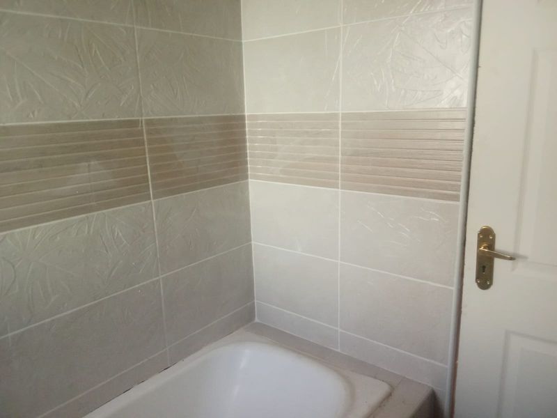A bathroom corner featuring a built-in bathtub with decorative ceramic wall tiling and a standard interior door.