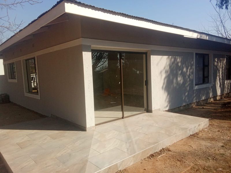Rear view of the property featuring a tiled patio, sliding glass doors, and modern aluminium window frames with a clean plastered exterior finish.