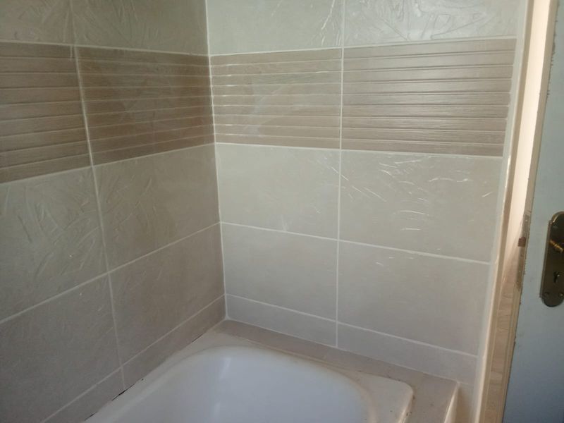 A bathroom corner featuring a built-in bathtub with neutral-toned decorative ceramic wall tiles.