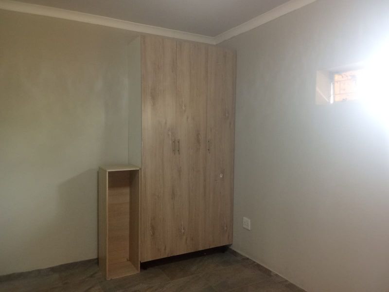 A clean, empty bedroom featuring a modern light wood-finish built-in wardrobe and neutral wall tones.