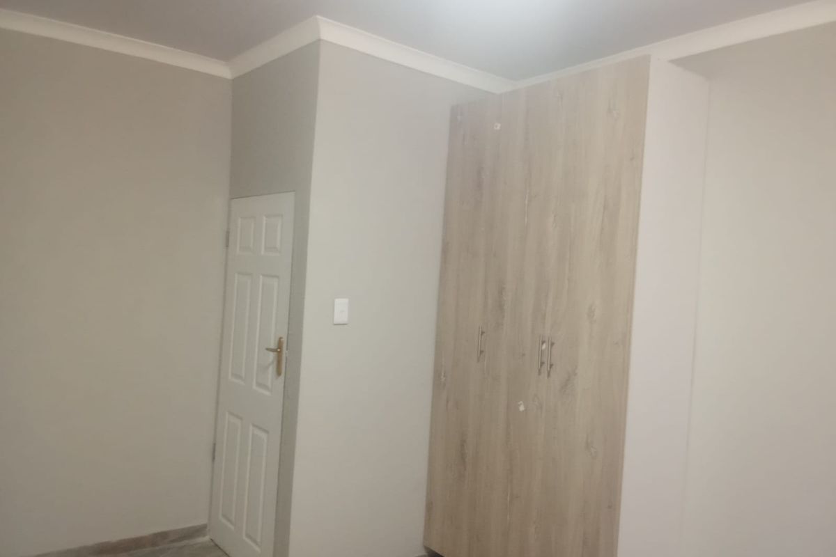 A clean, empty bedroom featuring neutral wall tones, tiled flooring, and a modern built-in wardrobe with light wood-grain finish.