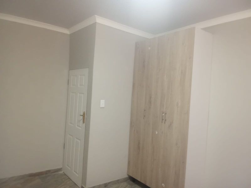 A clean, empty bedroom featuring neutral wall tones, tiled flooring, and a modern built-in wardrobe with light wood-grain finish.