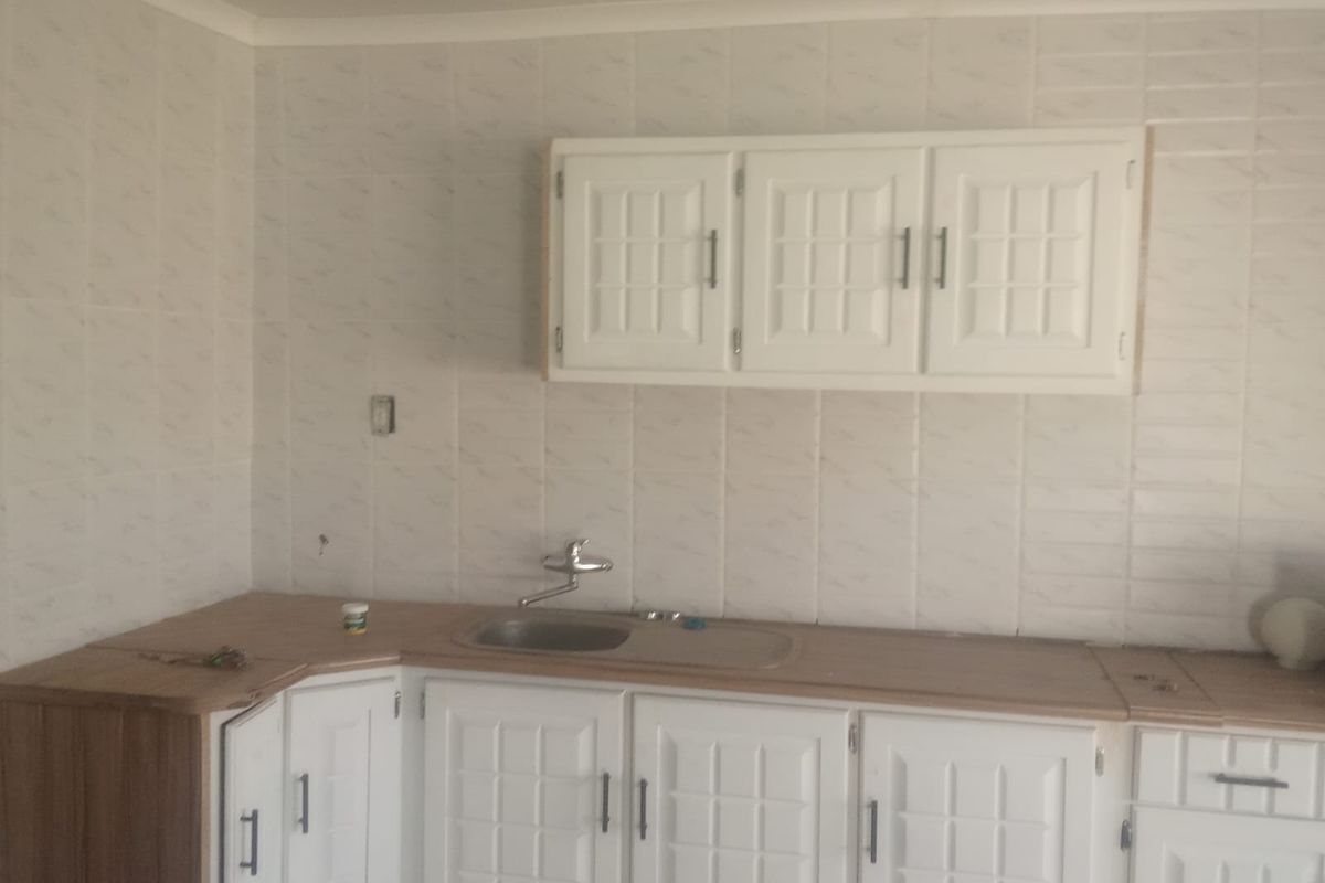 A functional kitchen area featuring white cabinetry, laminate countertops, and a stainless steel sink with tiled splashback, requiring minor electrical finishing.