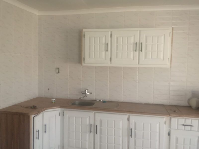 A functional kitchen area featuring white cabinetry, laminate countertops, and a stainless steel sink with tiled splashback, requiring minor electrical finishing.