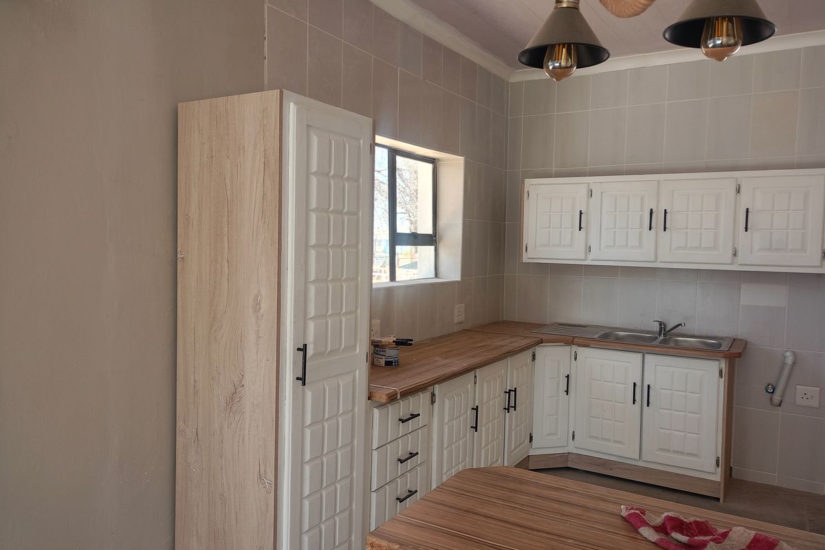 A functional kitchen featuring white built-in cabinetry, wood-look laminate countertops, a stainless steel sink, and tiled splashbacks.