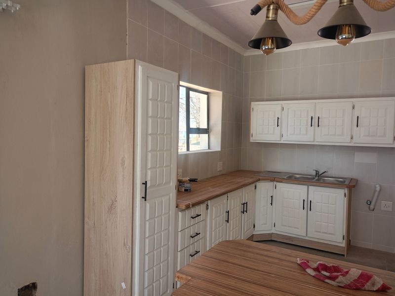 A functional kitchen featuring white built-in cabinetry, wood-look laminate countertops, a stainless steel sink, and tiled splashbacks.