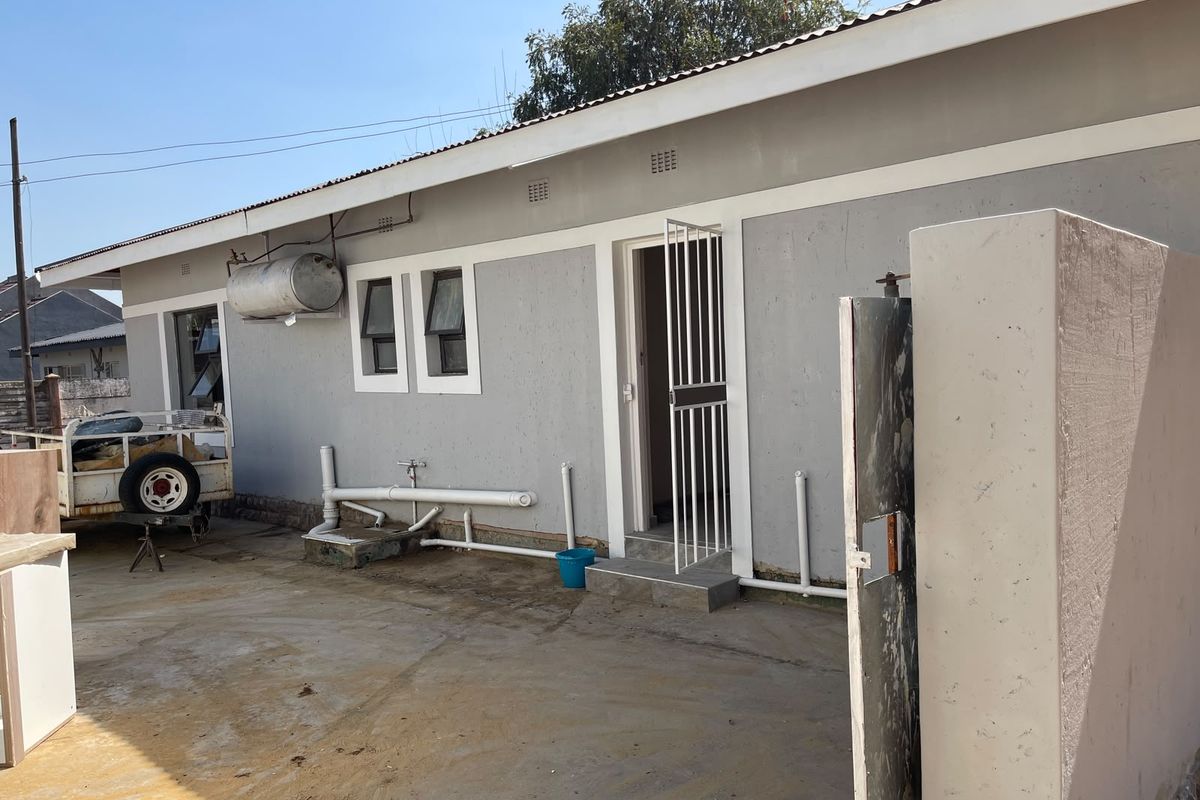 Rear exterior view of the property featuring a concrete driveway, security gate, and external plumbing fixtures with a solar geyser installed.