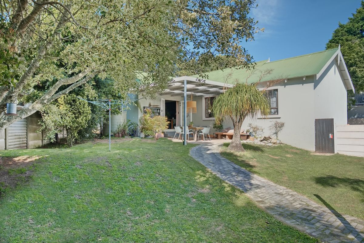 Rear view of the house featuring a green corrugated roof, a paved garden path, and a covered patio area overlooking the lawn.