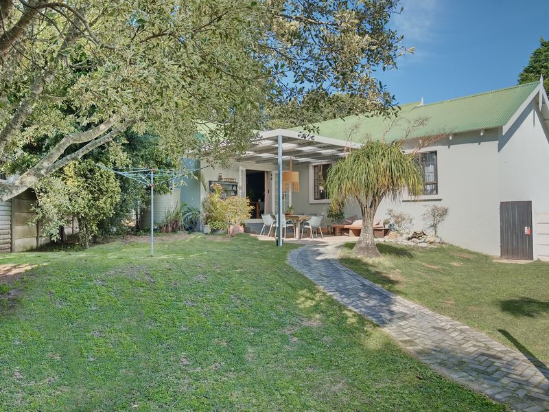 Rear view of the house featuring a green corrugated roof, a paved garden path, and a covered patio area overlooking the lawn.