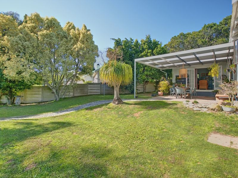 A well-maintained rear garden featuring a spacious covered patio area, paved pathways, and established trees, providing a private outdoor living space.